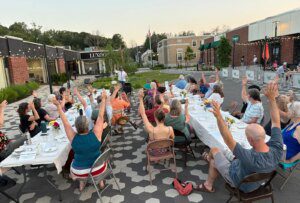 Community members raise their arms during a gratitude poem at a supper in Westbrook, Maine, in July 2025 [Courtesy of Community Plate]