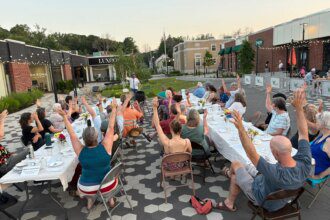 Community members raise their arms during a gratitude poem at a supper in Westbrook, Maine, in July 2025 [Courtesy of Community Plate]